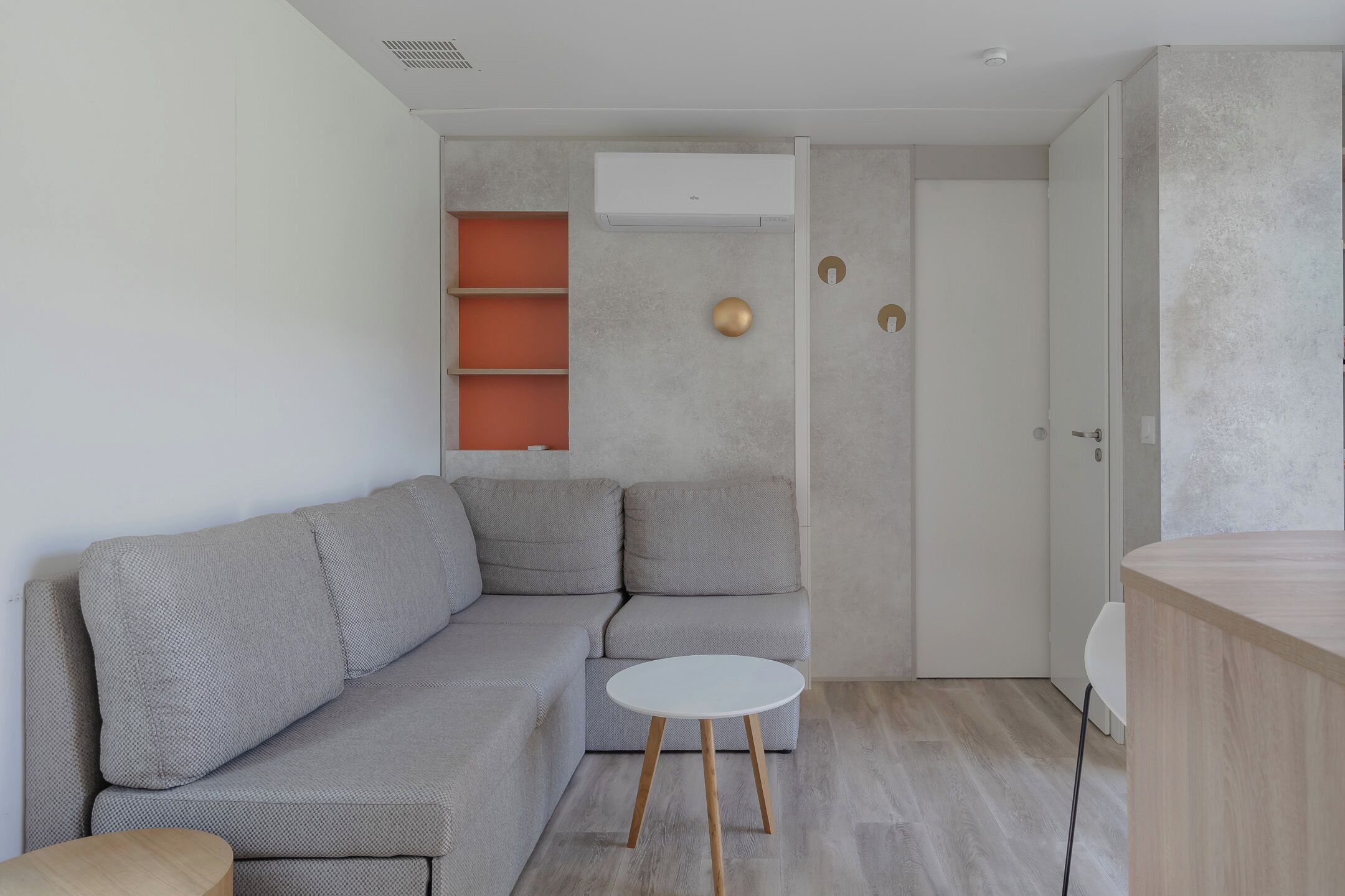 A modern living room with a grey sectional sofa, a small white round table, and a wooden side table.