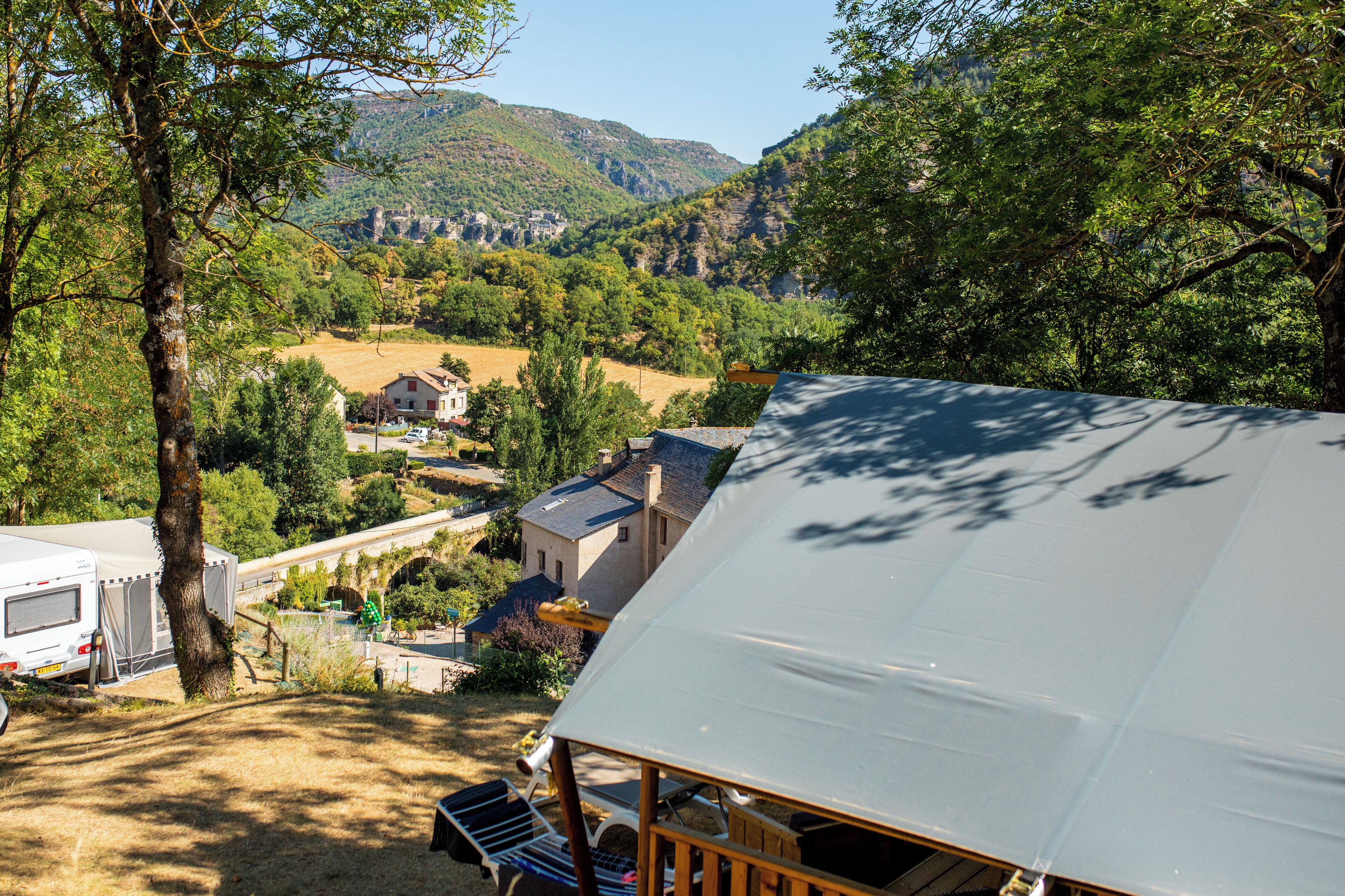 A campsite with tents and a small building, surrounded by trees and a mountainous landscape.