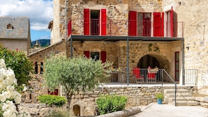 Un bâtiment en pierre avec des volets rouges, un balcon et un petit jardin.