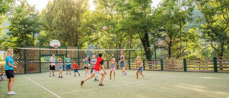 Una cancha de tenis con jugadores en juego, rodeada de árboles y una valla.