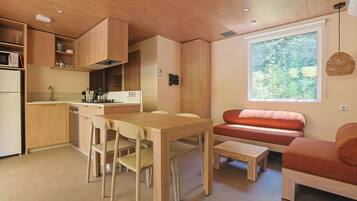 Cocina compacta con armarios de madera, una mesa de comedor con sillas, una pequeña isla de cocina y una ventana con vistas a zonas verdes.
