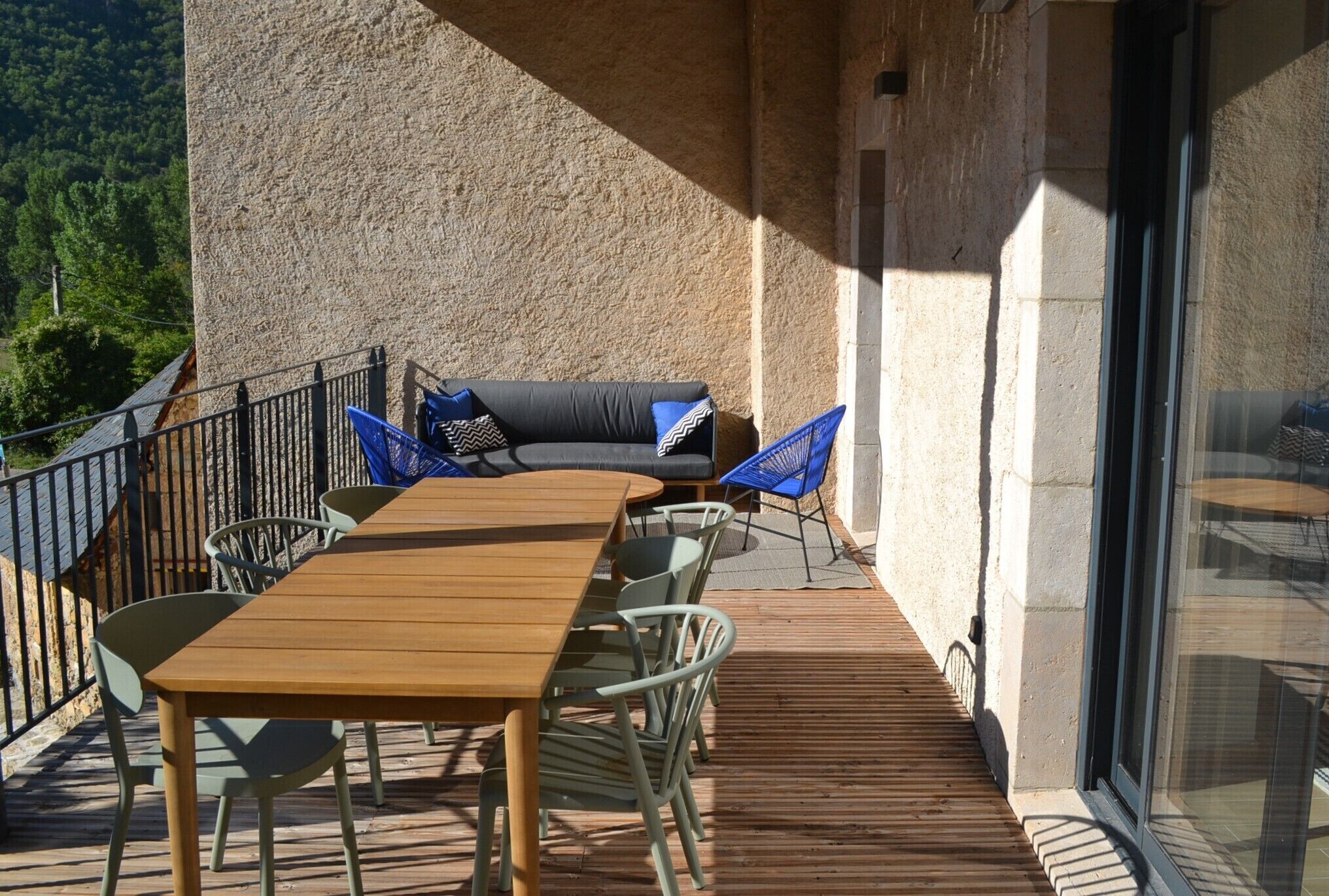 An outdoor patio with a wooden table and chairs, a sofa, and a glass door.