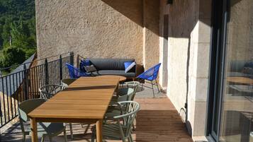 An outdoor patio with a wooden table and chairs, a sofa, and a glass door.