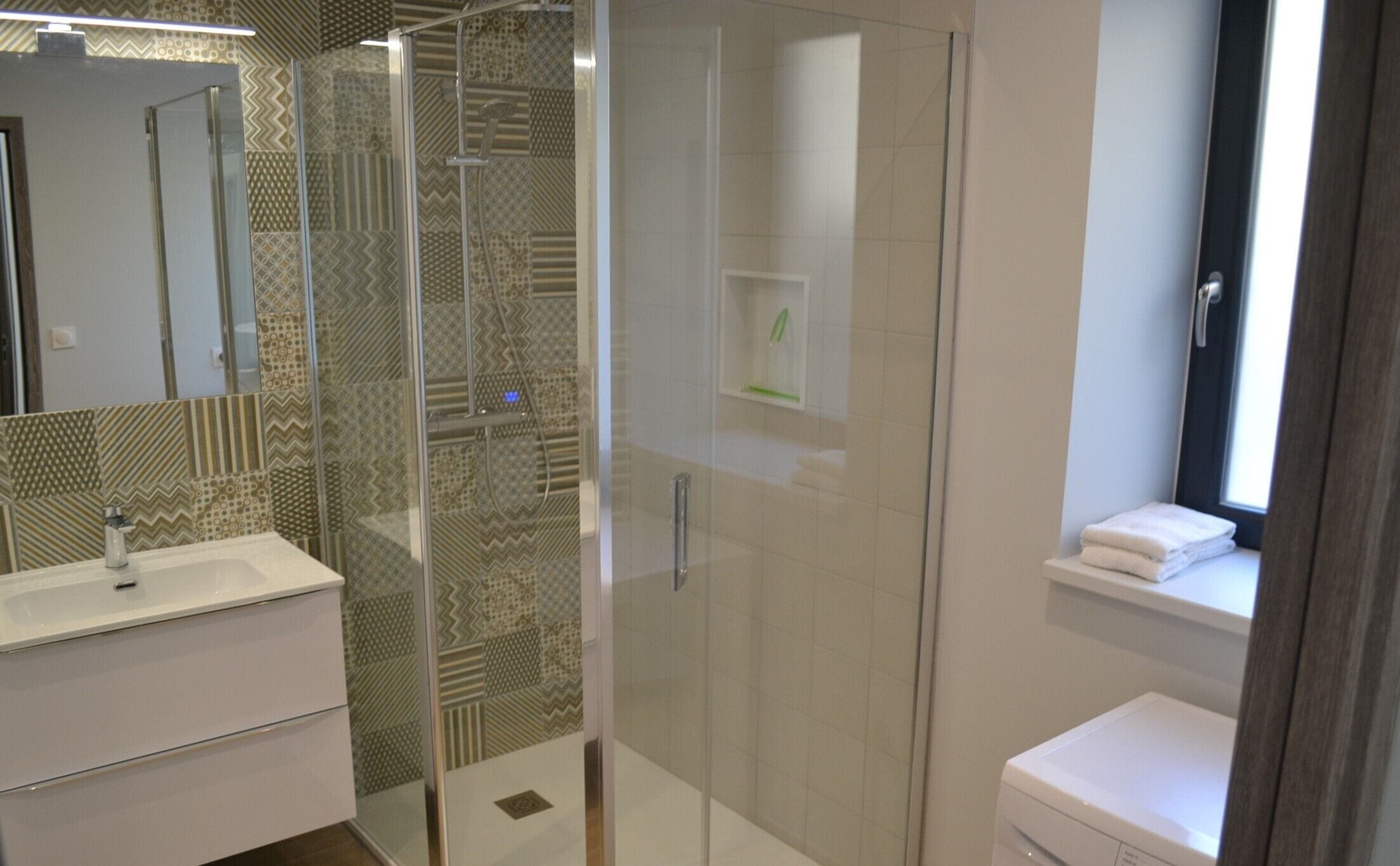 A modern bathroom with a glass shower enclosure, a white sink, and a window above the toilet.
