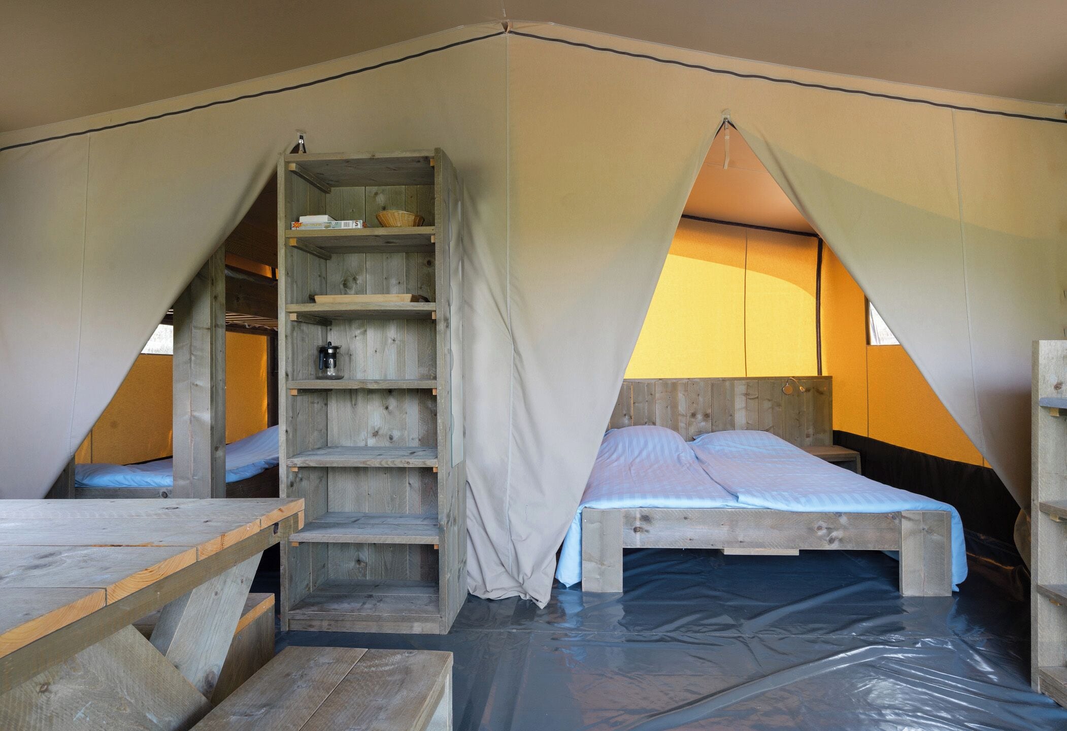 A tented accommodation with a wooden bed, a built-in shelf, and a table.