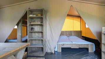 A tented accommodation with a wooden bed, a built-in shelf, and a table.