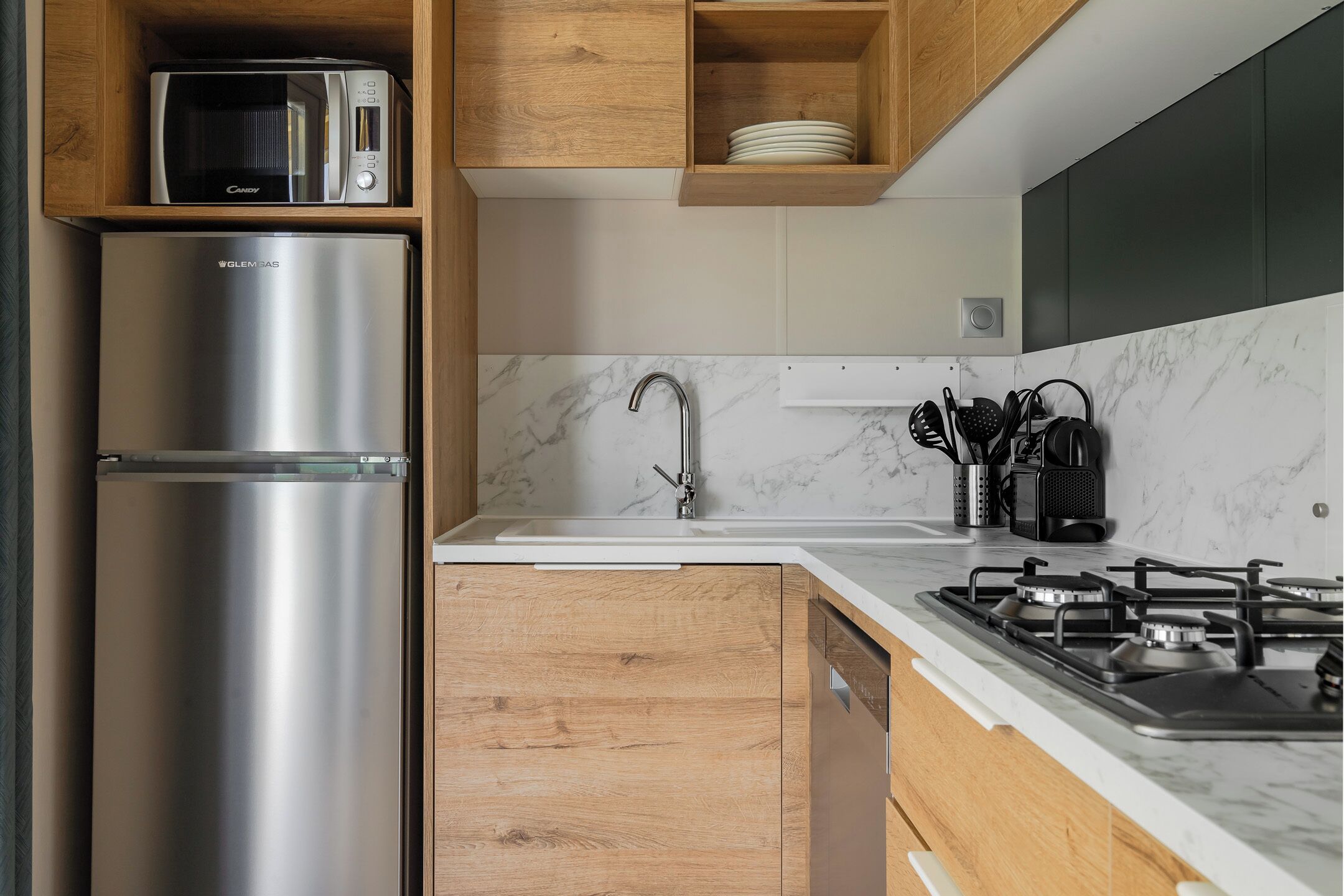 A modern kitchen with a stainless steel refrigerator, a microwave, a gas stove, and wooden cabinets.