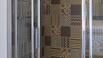 A shower with a glass door and patterned tiles.