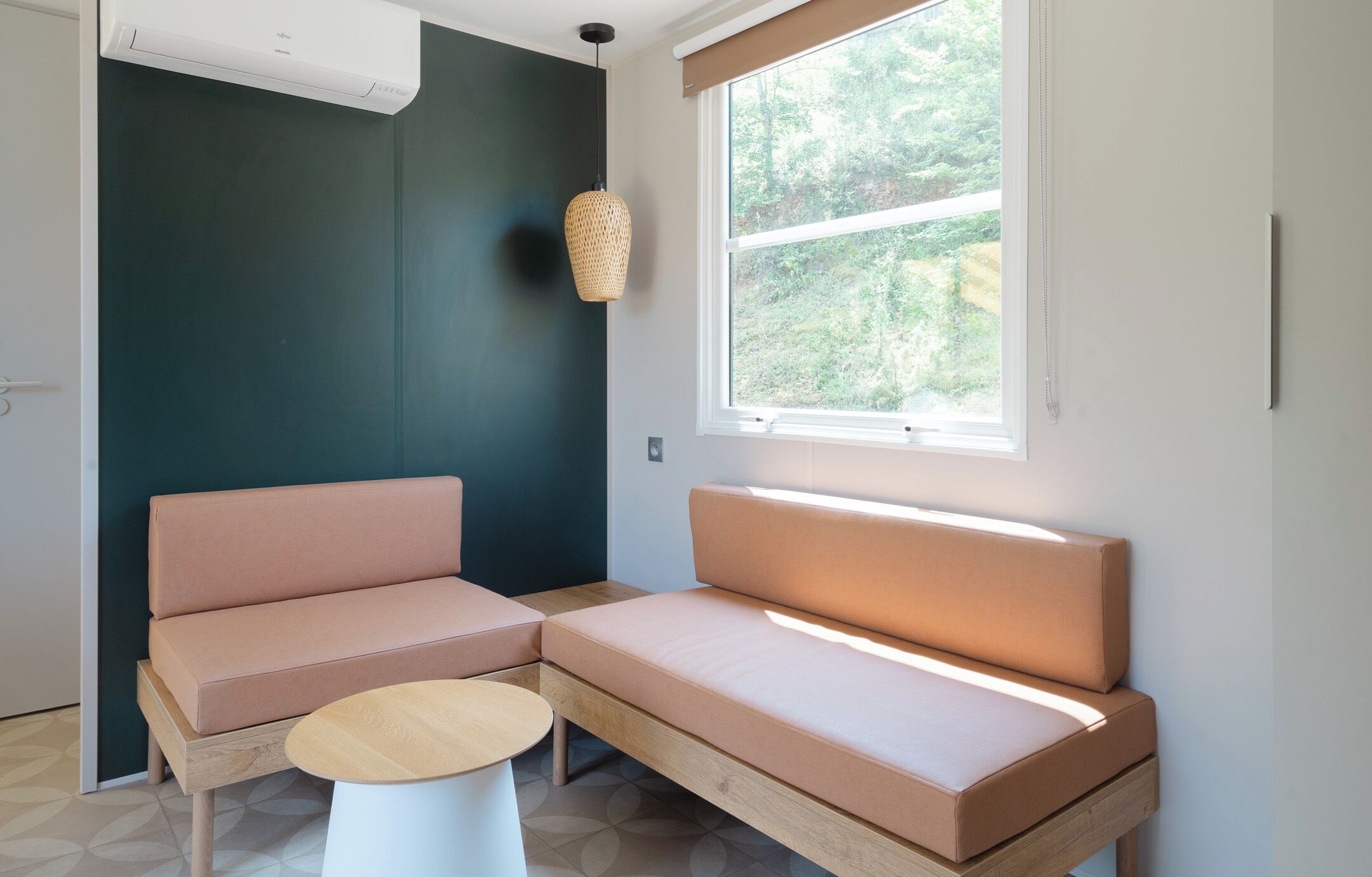 A modern room with a sectional sofa, a small round table, and a large window with a view of greenery.