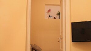 A room with a bed, a chair, a television, and a small table with flowers. - Arco Suite (Lecce)