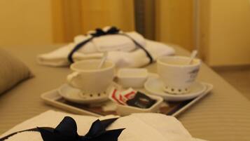A neatly arranged hotel room with a bed, pillows, a tray with cups and a spoon, and a towel with a black ribbon.