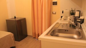 A compact kitchen with a stainless steel sink, a small refrigerator, and a dining area with a table. - Arco Suite (Lecce)