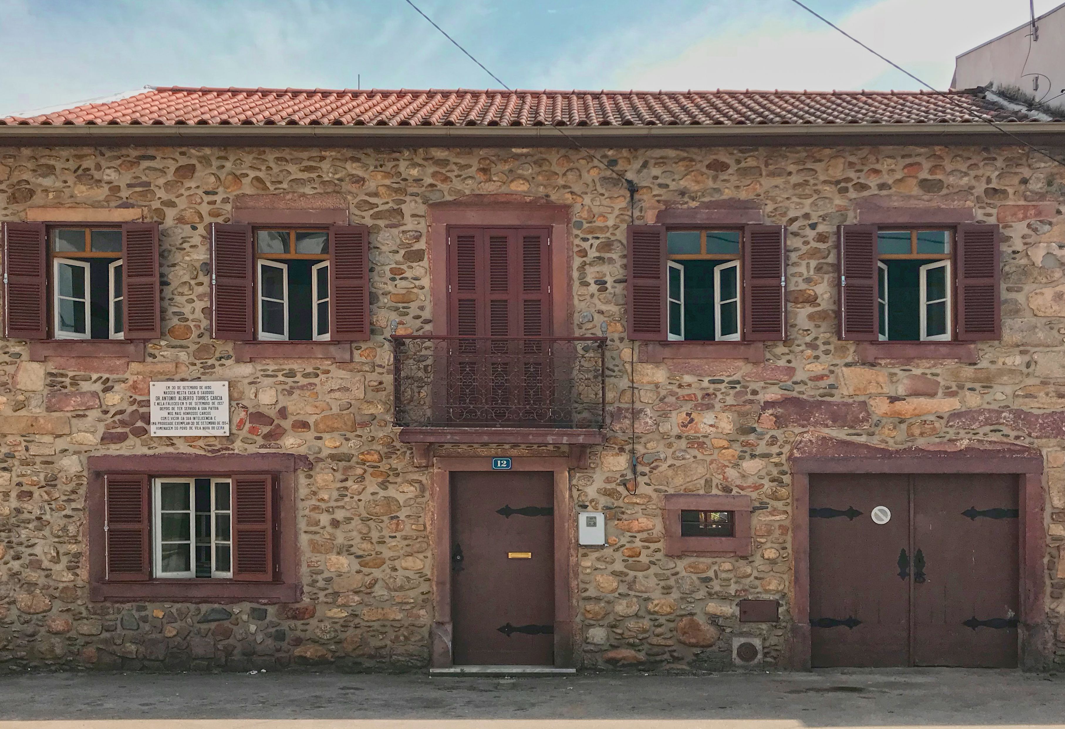 A stone building with multiple windows and doors, a balcony, and a sign. - Portantiqua Guest House (Góis)