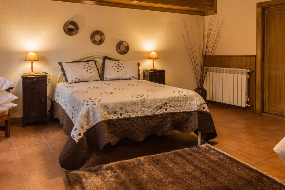 A bedroom with a bed, two bedside tables with lamps, a radiator, and a wooden door.