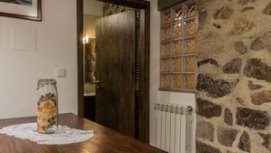 A wooden table with a glass jar containing dried flowers, a lace doily, and a stone wall with a window. - Portantiqua Guest House (Góis)