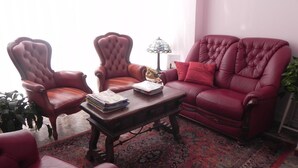 Una sala de estar con un sofá de cuero rojo, dos sillones, una mesa de centro de madera y una alfombra estampada.