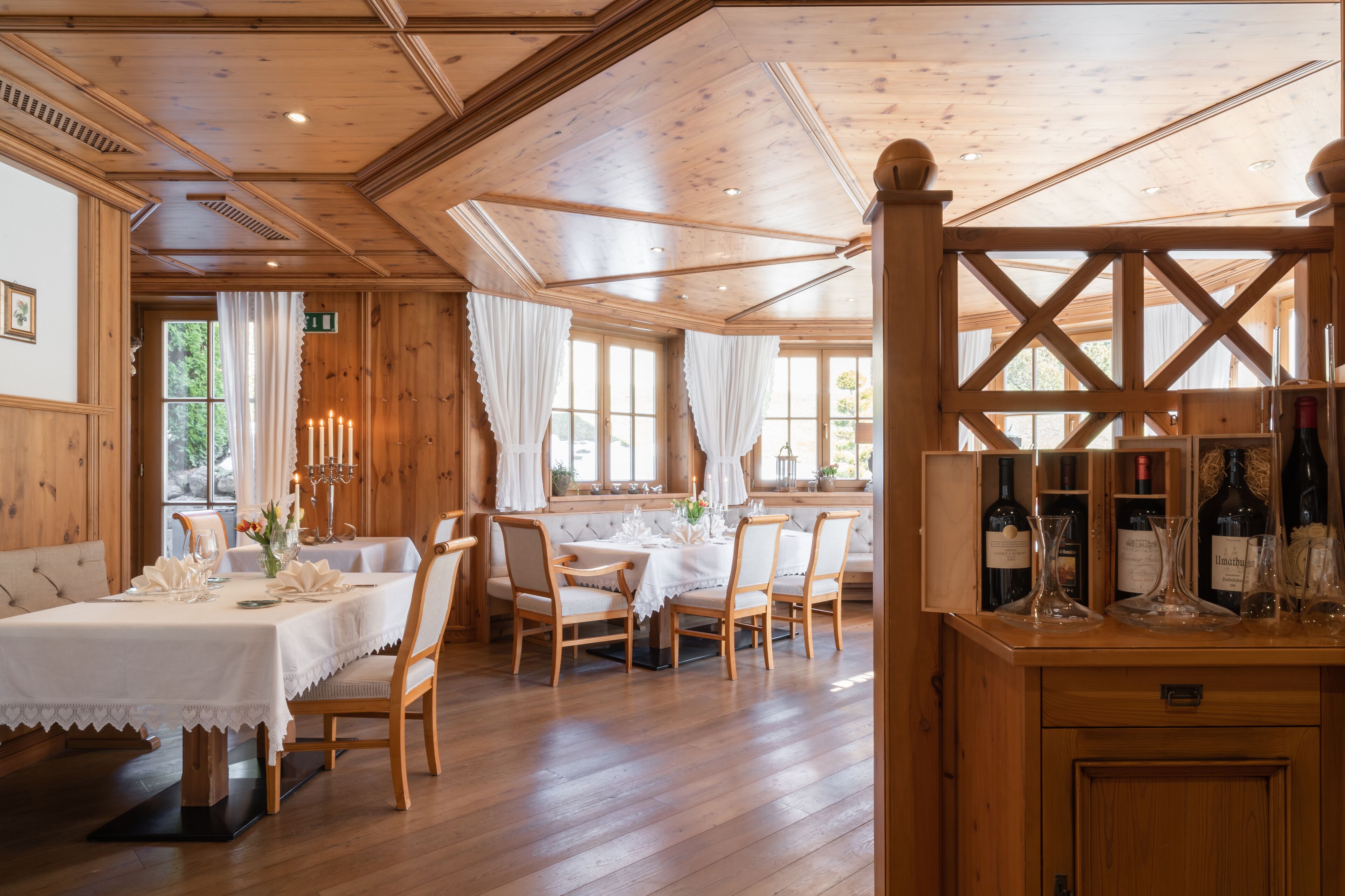 A wooden dining room with a table set for four, a wine rack, and a view of the outdoors through large windows.