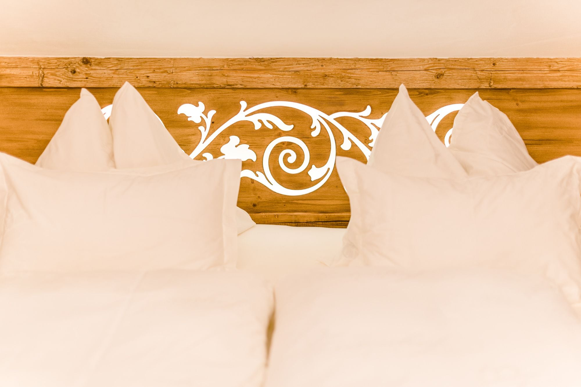 A bed with white bedding and pillows, a wooden headboard with a floral design, and a plain wall.