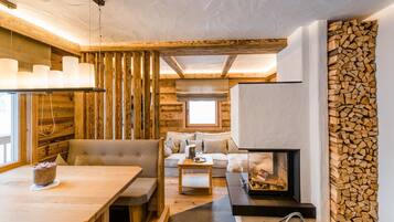 L’intérieur chaleureux d’un chalet avec une table à manger en bois, des sièges confortables, une cheminée et un mur en rondins.