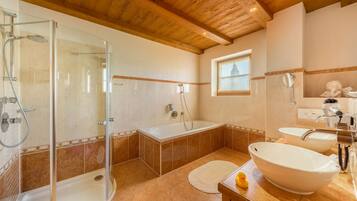 A bathroom with a glass-enclosed shower, a bathtub, and two sinks.