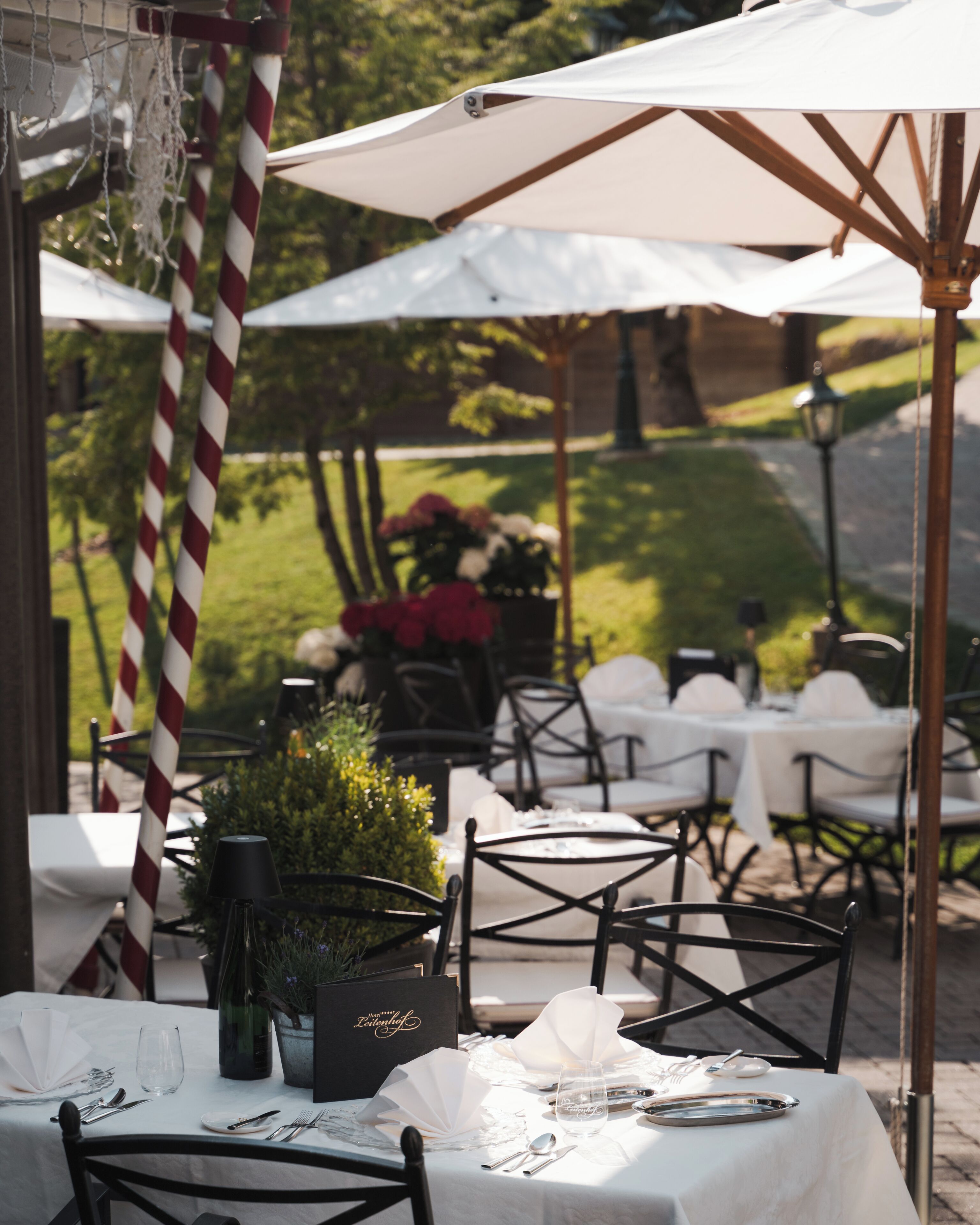 An outdoor dining area with tables set for two, white tablecloths, and red and white striped poles.
