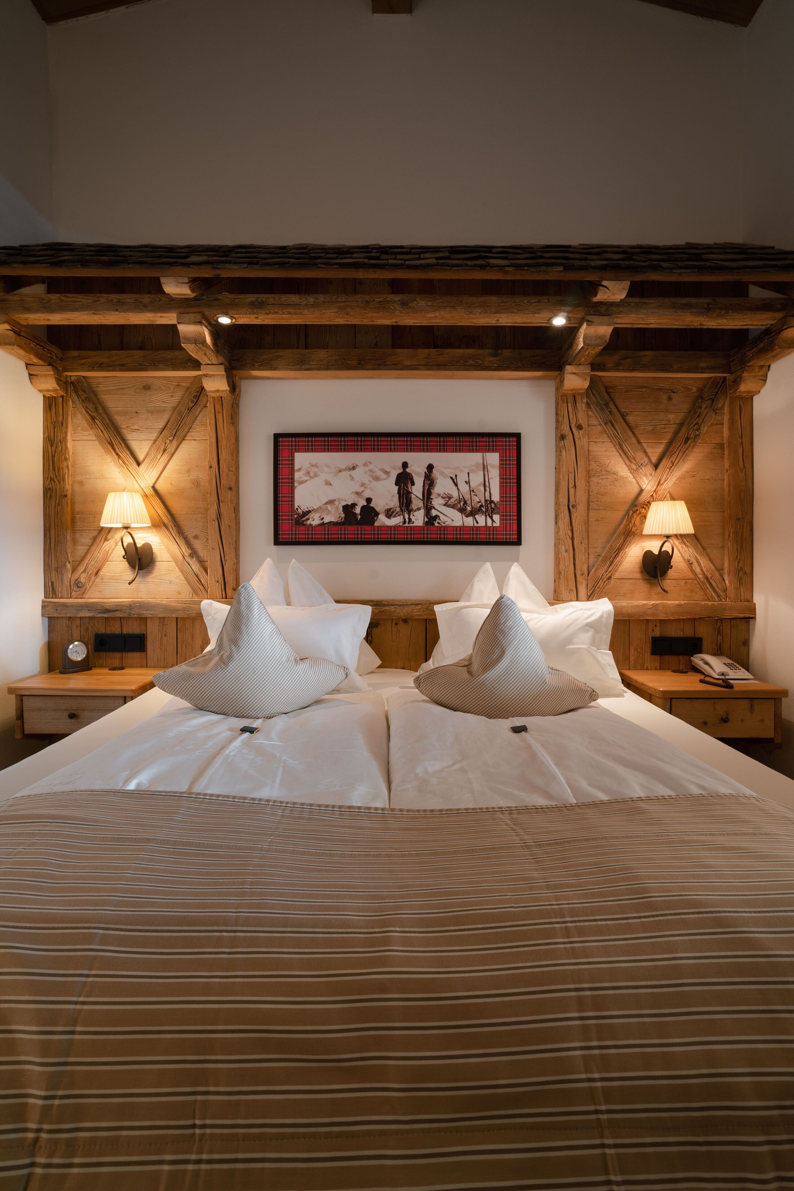 A hotel room with a large bed, wooden headboard, two bedside tables with lamps, and a framed picture on the wall.