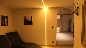 Une chambre avec un lit, une table de chevet, une tête de cerf accrochée au mur, et un couloir menant à une autre pièce.