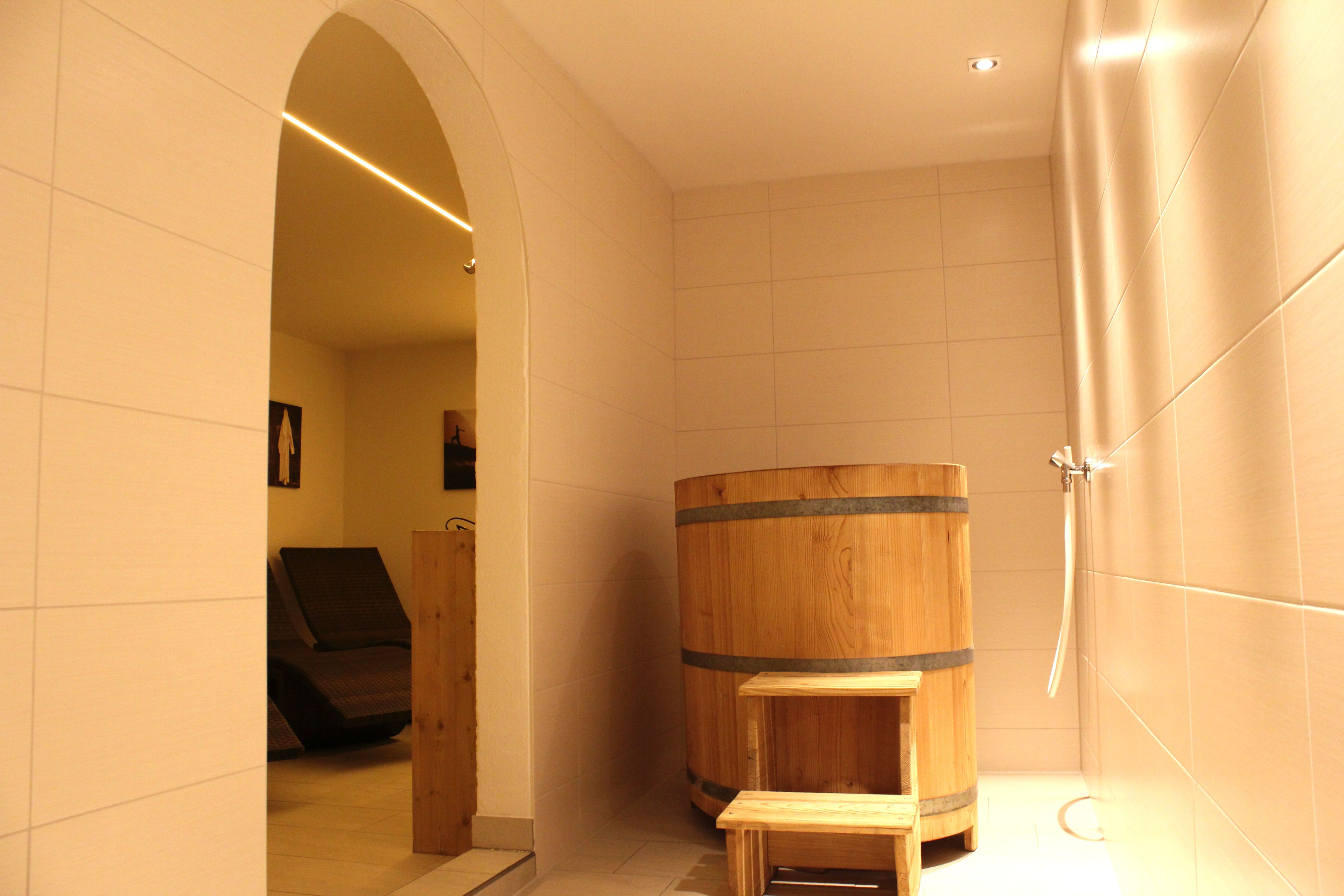 A bathroom with a wooden barrel, a bench, and a shower area.