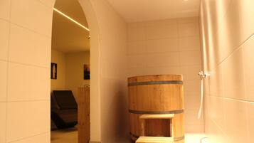 A bathroom with a wooden barrel, a bench, and a shower area.