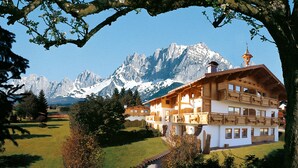 Un chalet traditionnel en bois, doté de plusieurs balcons, qui se dresse sur fond de montagnes enneigées.