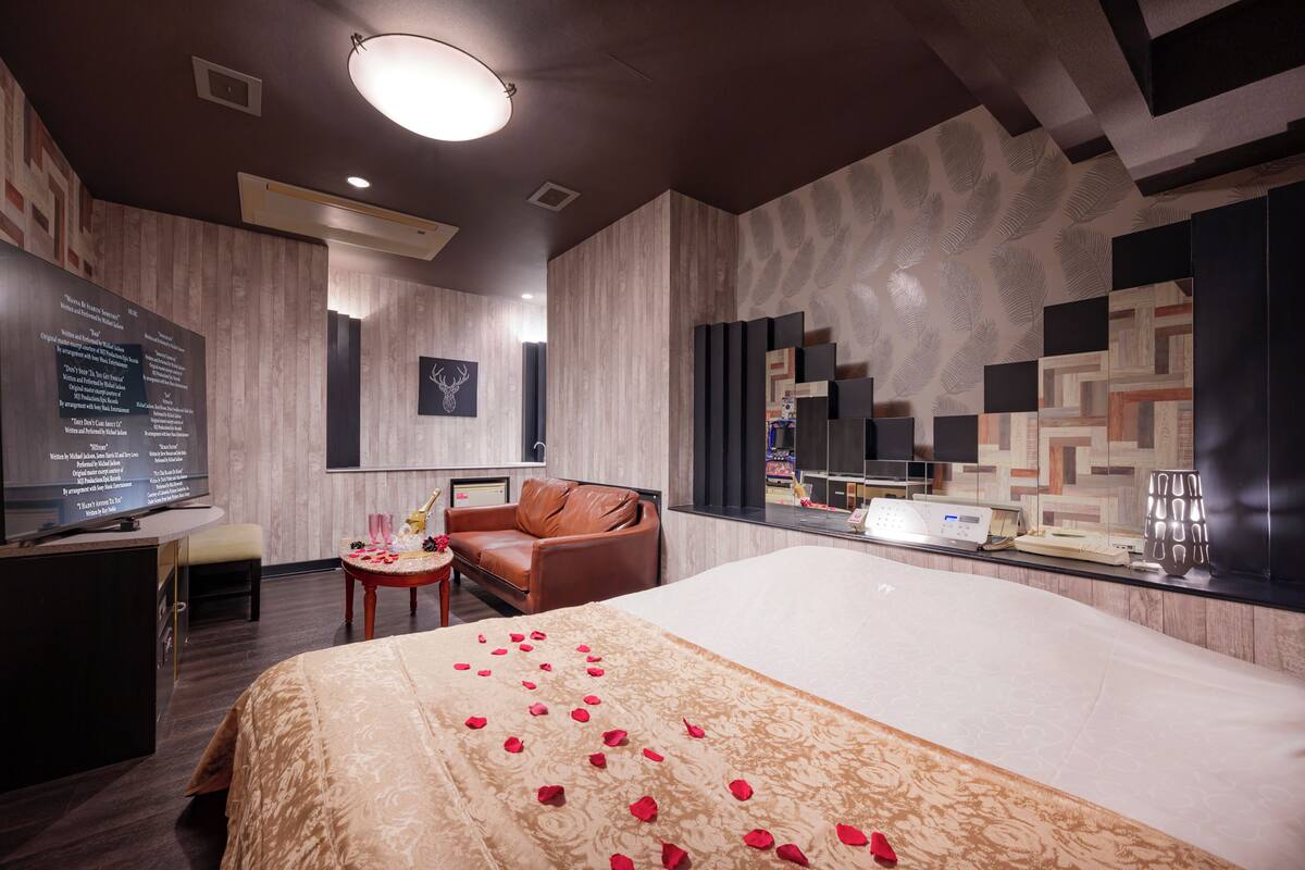 A hotel room with a large bed, a leather sofa, a small table, and a TV.