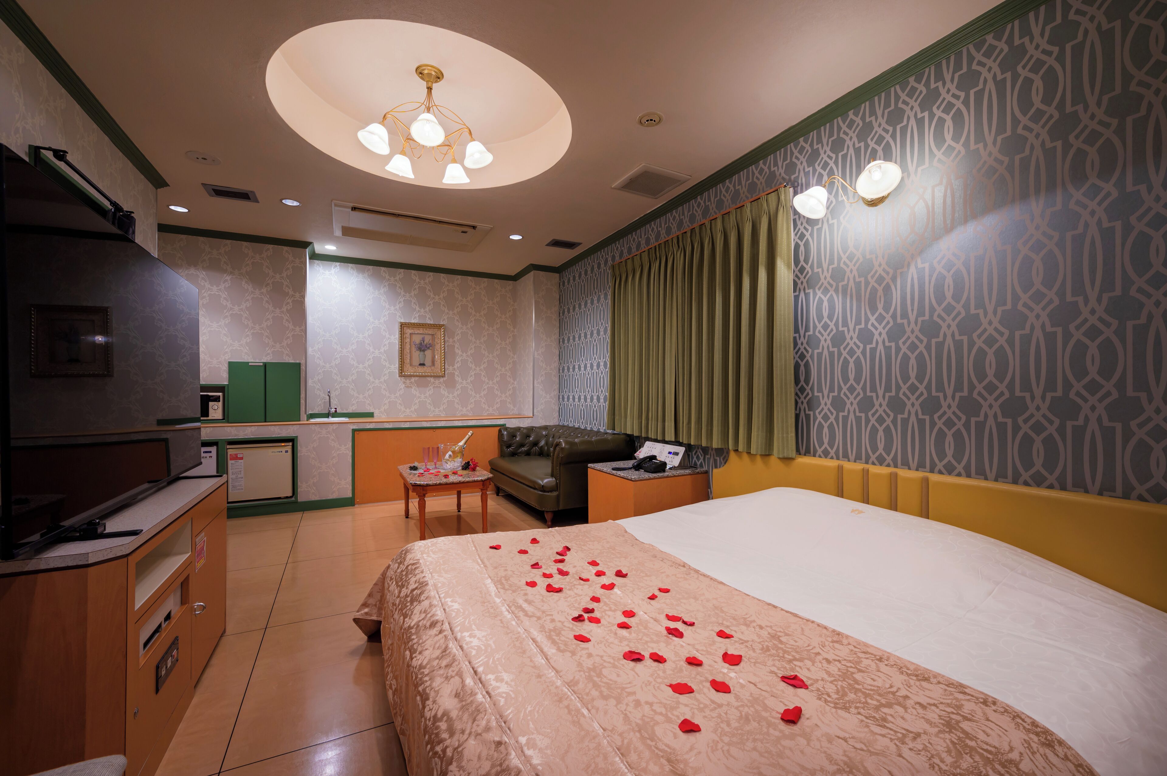 A hotel room with a bed, a desk, a television, a green sofa, and a patterned wall.