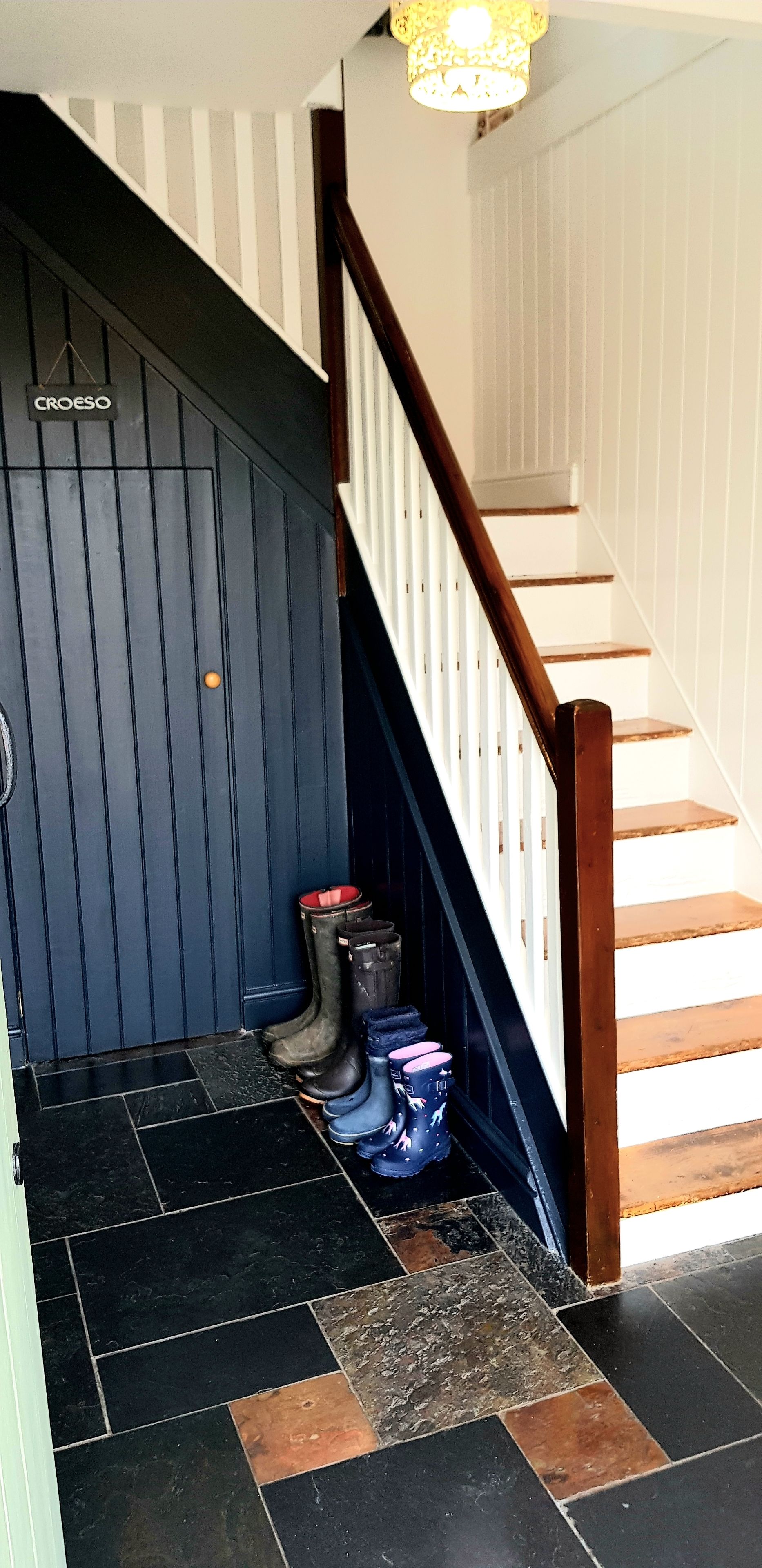 Un escalier avec une rampe en bois et un mur noir sur lequel est inscrit le mot « CROESO ».