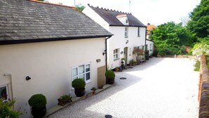 A narrow street lined with white houses with dark roofs, gravel driveways, and potted plants. - Vale View Cottages - The Coach House (Prestatyn)