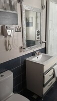 A bathroom with a toilet, sink, and mirror. There is a telephone mounted on the wall.