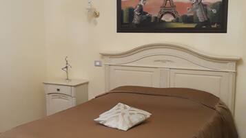 A bedroom with a bed, a nightstand, a bench, a painting of the Eiffel Tower, and a small table with a lamp.