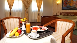 Quarto de hotel com bandeja de café da manhã em uma mesa, incluindo frutas, um copo de suco e uma xícara de café.
