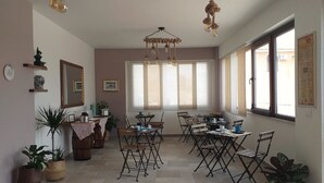 Een eetruimte met tafels en stoelen, grote ramen en hanglampen.