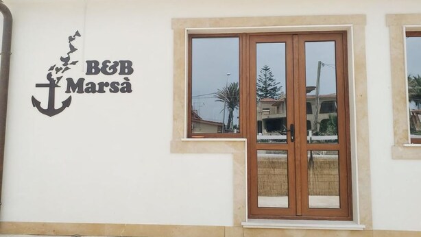 Een gebouw met een bord waarop 'B&B Marsa' staat en een houten deur met ruiten.