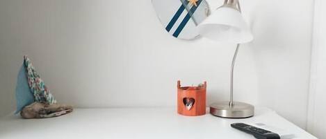 A white desk with a wall-mounted lamp, a remote control, and a decorative item.