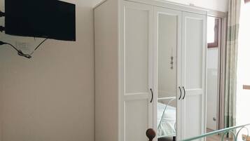 Una habitación con un armario blanco, un televisor de pantalla plana montado en la pared y una puerta de cristal que da a otra habitación.