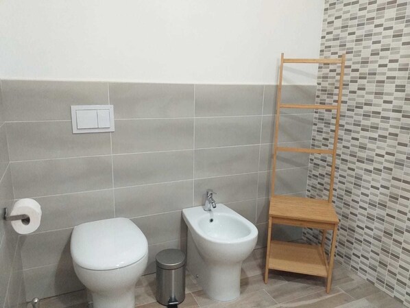 Une salle de bain équipée de toilettes, d’un bidet et d’une étagère en bois.