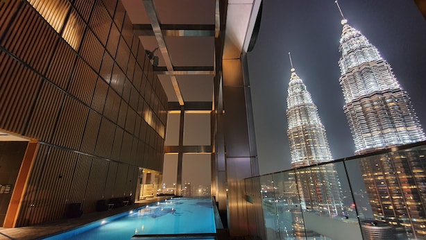 Een modern gebouw met een glazen gevel, een zwembad en uitzicht op de Petronas Towers.