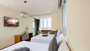 Habitación de hotel con dos camas, un escritorio, una silla, un televisor y vista al mar.