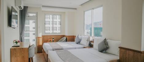 Habitación de hotel con dos camas, un escritorio, una silla, un televisor y una ventana con vistas a edificios.
