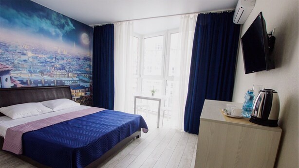Una camera d'albergo con un letto, una scrivania con un bollitore, una TV e una finestra con tende.