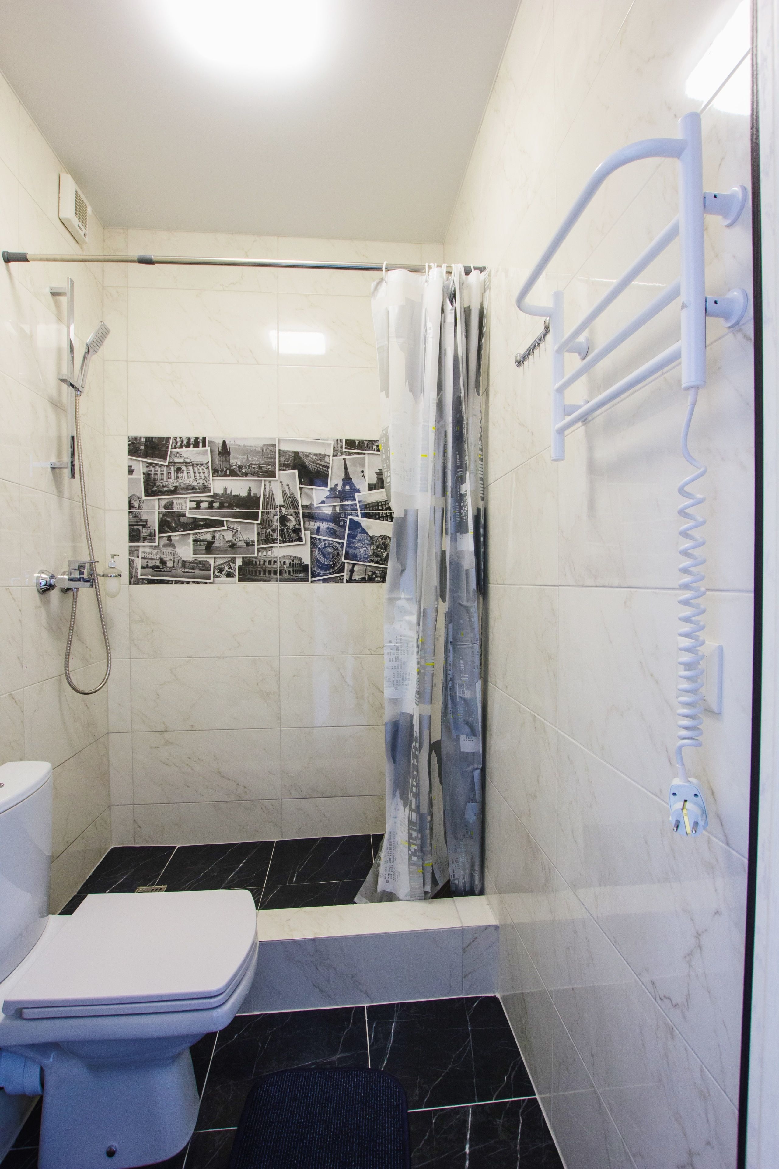 A bathroom with a shower, toilet, and a wall with black and white photos.