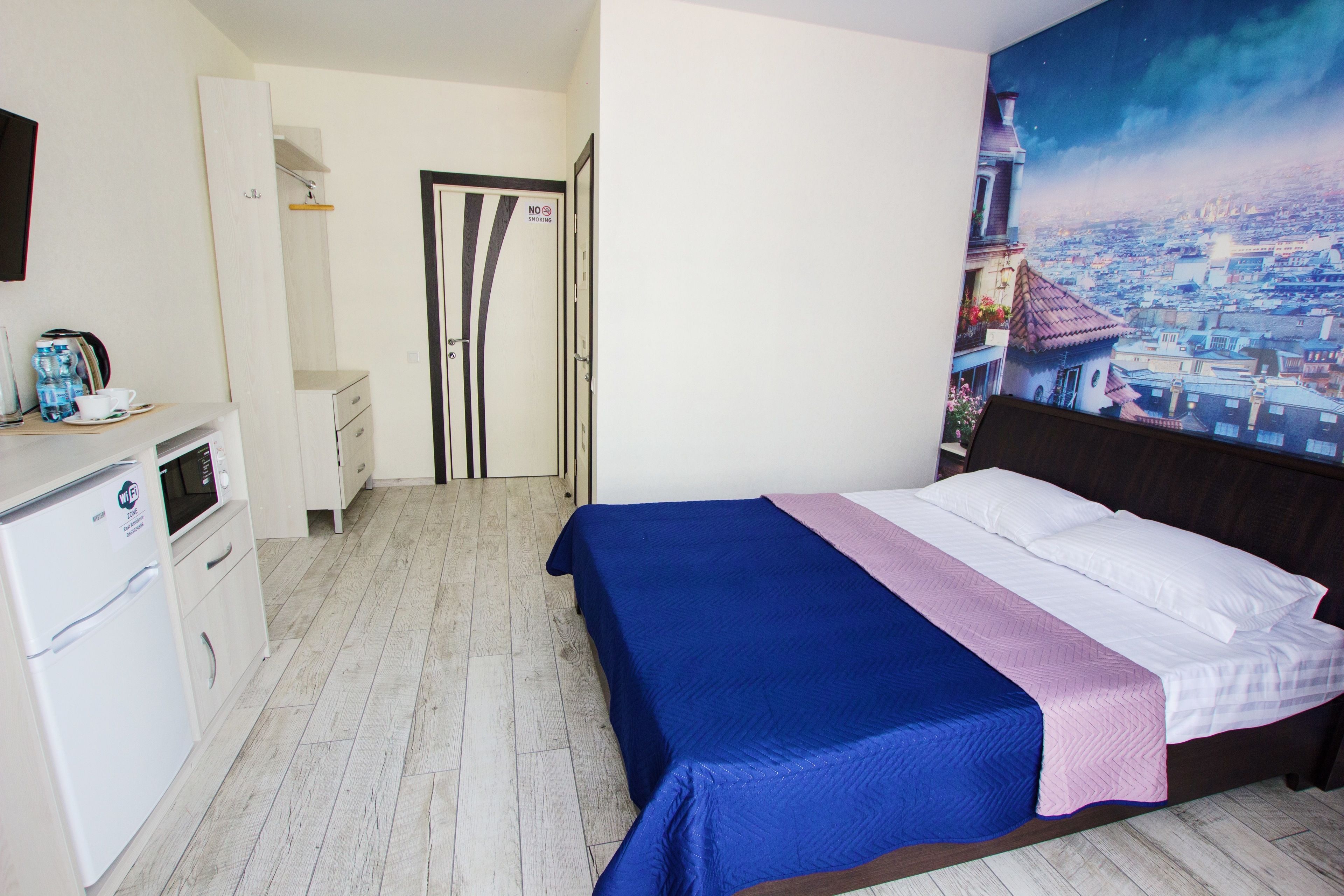 A bedroom with a bed, a desk with a computer, a microwave, and a refrigerator.