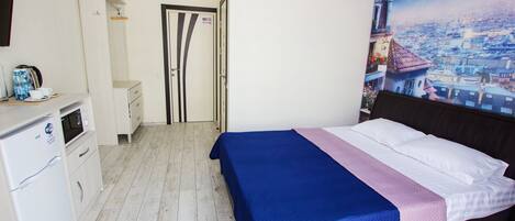 A bedroom with a bed, a desk with a computer, a microwave, and a refrigerator.