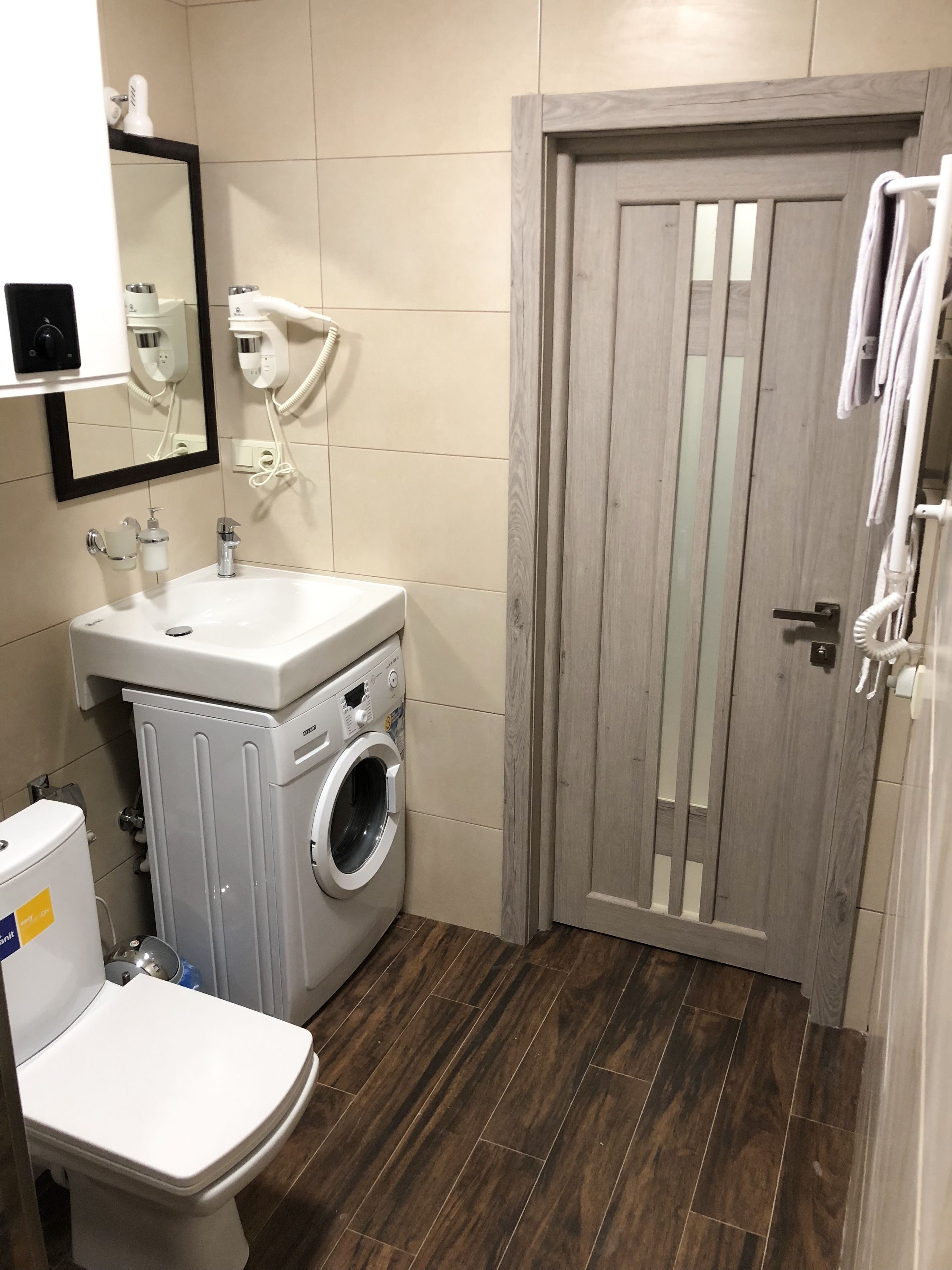 Un baño pequeño con inodoro, lavadora, lavabo y puerta de madera.